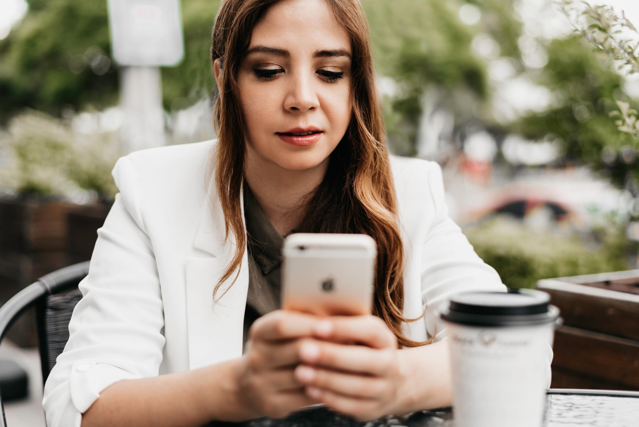 A person drinking coffee whilst using their mobile phone at a table