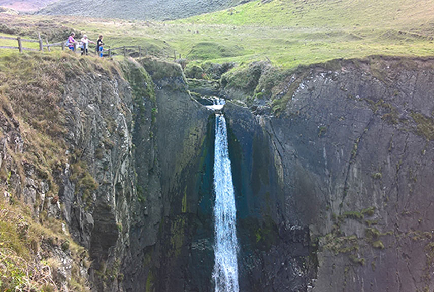 Waterfall surrounded by Green Devon Hills & Grey Cliffs with People Watching