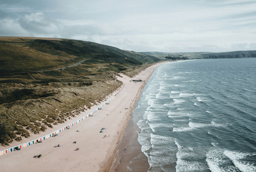 People & Beach Huts on the Sandy Woolacombe Beach backed by green Hills